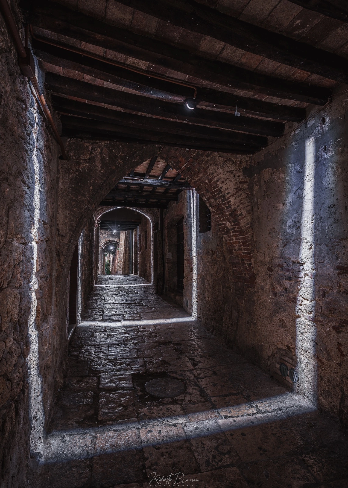 Vicoli — lame di luce, Massa Marittima — la sequenza dei passaggi illuminati · fotografia roberto biancu